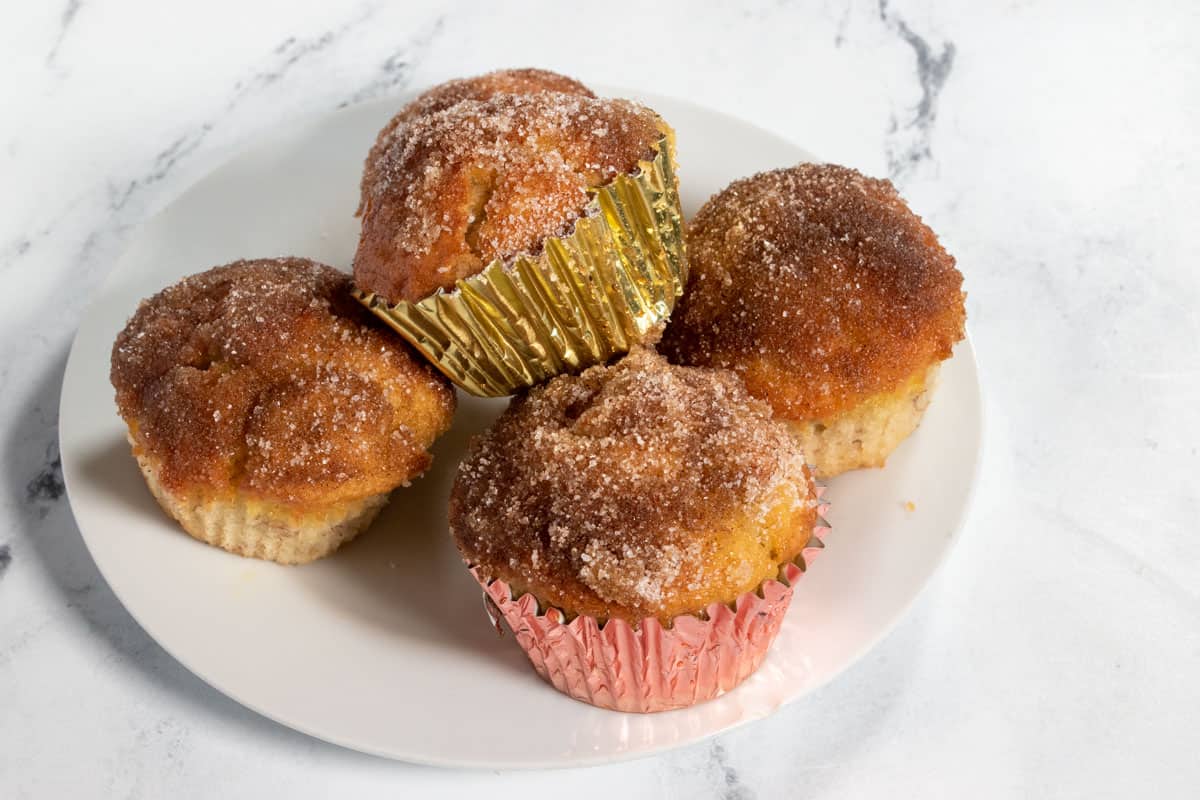 Four muffins after being dipped in the cinnamon sugar on a white plate.