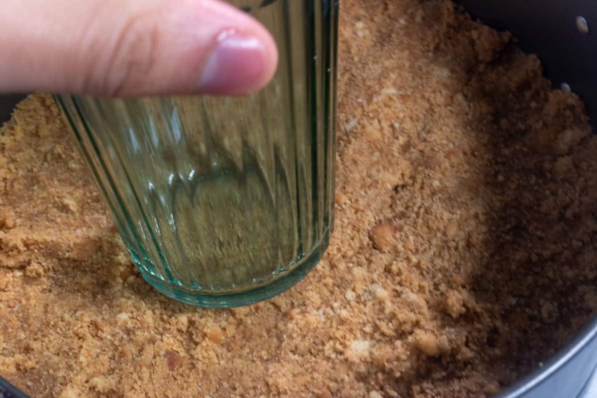 The crust being pressed into the baking tin with the bottom of a glass.