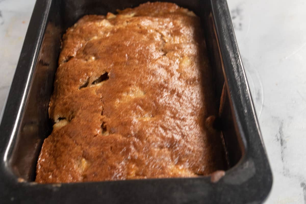 A golden brown baked apple cake inside one of the loaf cake tins. 