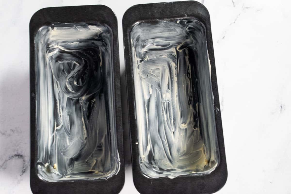 Two black loaf cake tins greased with vegan butter. 