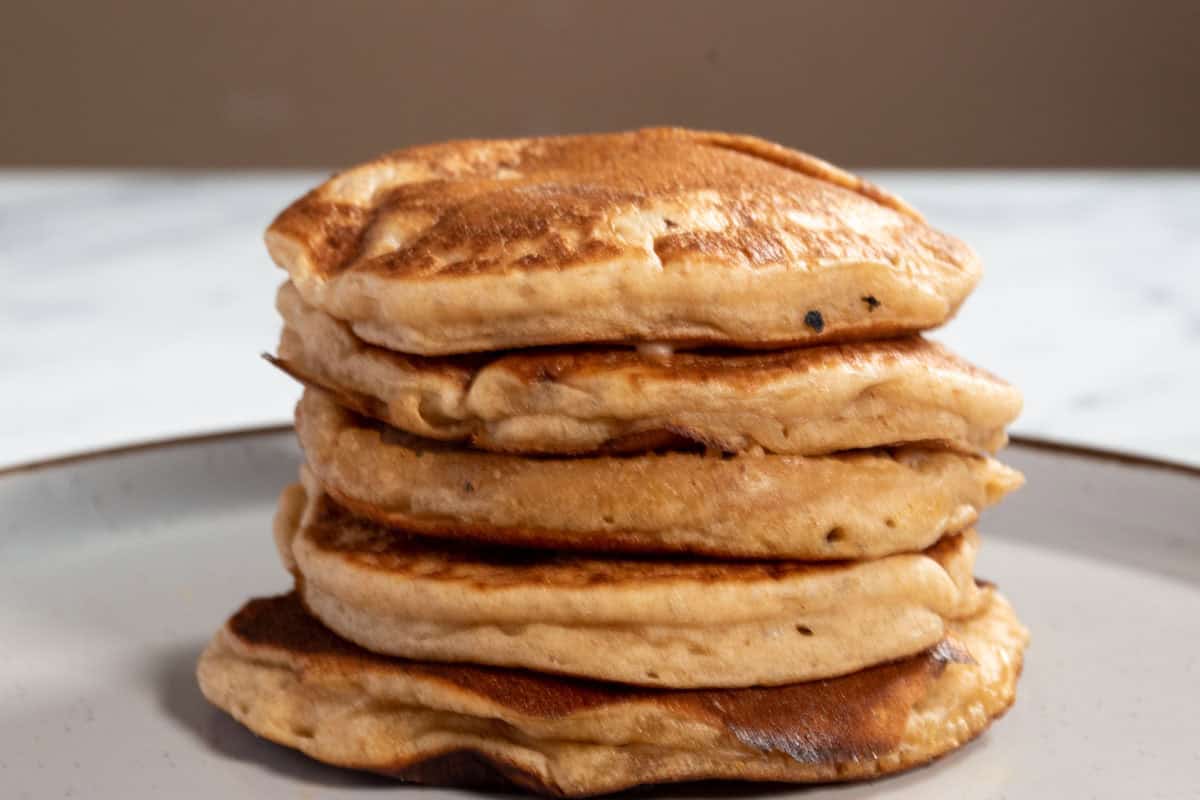 A golden stack of puffy vegan protein pancakes on a brown-rimmed white plate. 